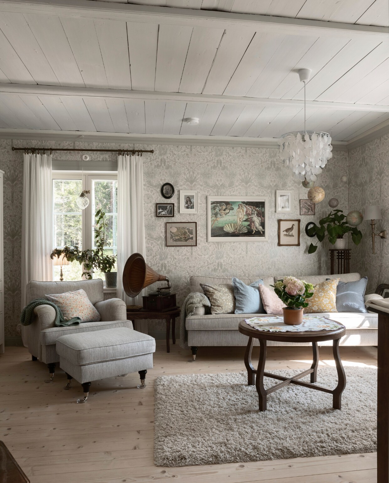 De woonkamer heeft ramen in twee richtingen. Een charmante oude platenspeler, gevonden op een rommelmarkt, was een kerstcadeau van Jenny’s ouders.Hij dient als decoratie, maar speelt nog steeds oude platen af.De bank en fauteuil in Howard-stijl zijn gekocht bij Kodin1.Het behang in de woonkamer is ‘Pure Honeysuckle & Tulip’ van William Morris. vtwonen Landelijk 06-2025 | styling, fotografie & tekst Heikki Rautio | productie Studio Rautio