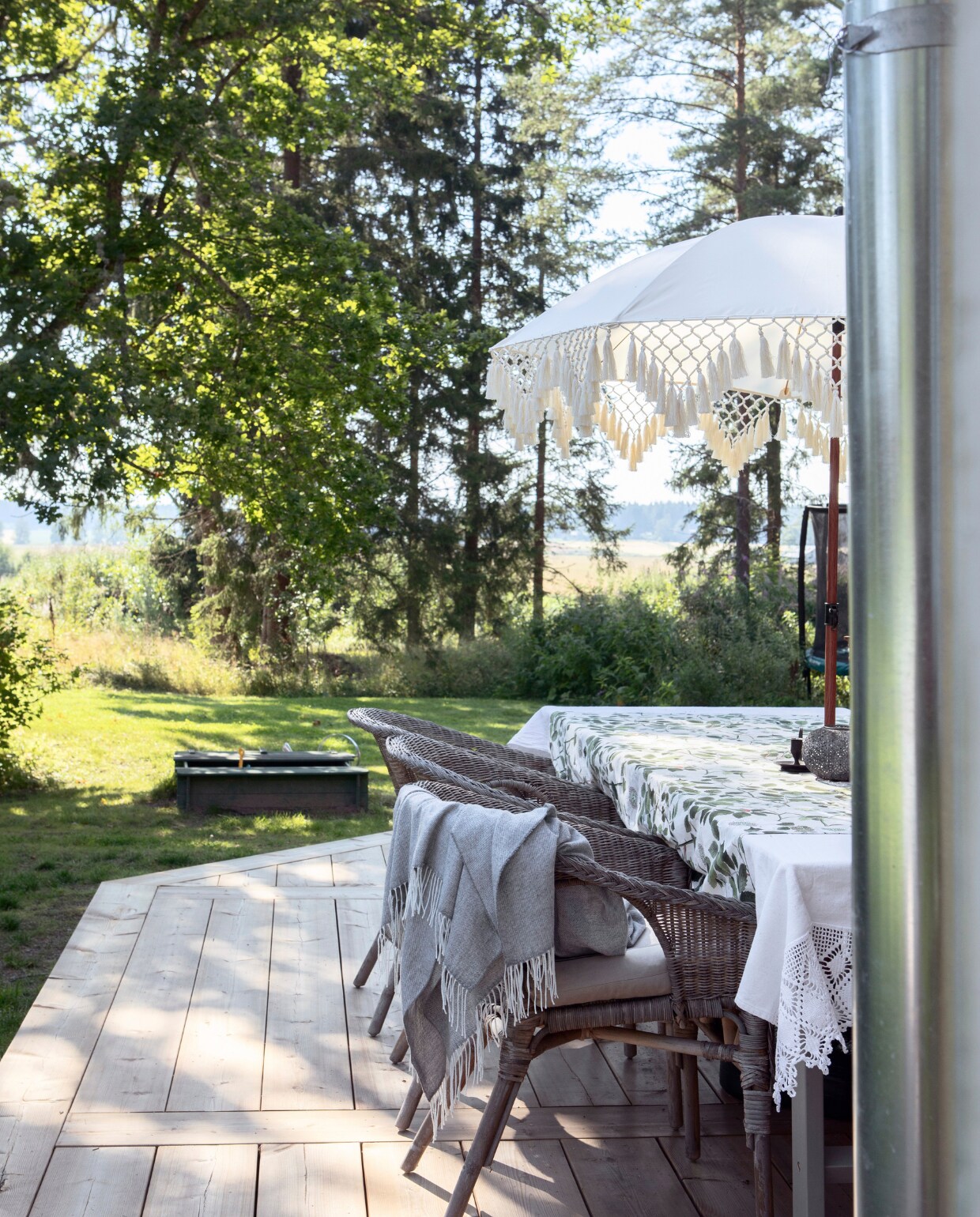 Vanaf een kleine heuvel aan het einde van het huis heb je uitzicht over uitgestrekte velden.In de zomer wordt er buiten gegeten en koffie gedronken wanneer het weer het toelaat. De terrasparasol werd gekocht in de outlethoek van de Comboliina-rommelmarkt. vtwonen Landelijk 06-2025 | styling, fotografie & tekst Heikki Rautio | productie Studio Rautio