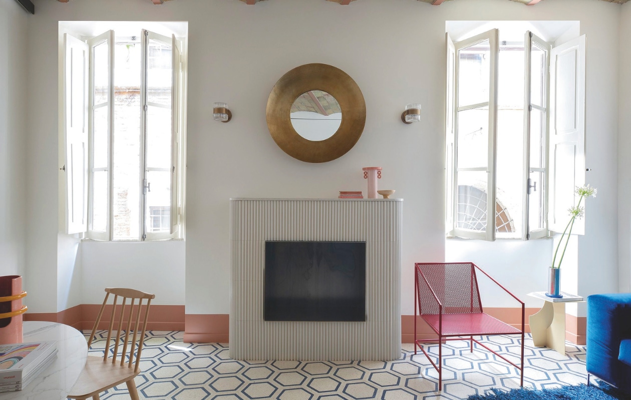 De haard is een ontwerp van Studio Tamat, bedekt met keramieken tegels van de broers Bouroullec. Wandlampen Soho Home. Houten stoel Hay. Stijlvol Wonen 04-2025 | styling Francesca Sironi | fotografie Monica Spezia | tekstbewerking Tanne Donjarcour Gielen | prouctie Living Inside | tekst Francesca Sironi