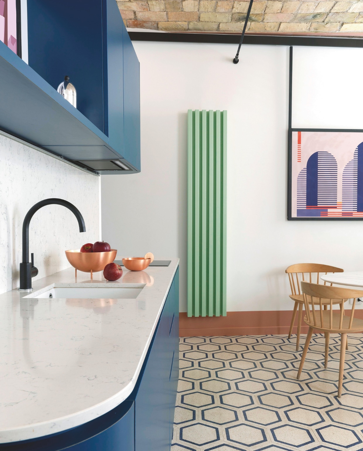 De keuken vormt het hart van de open woonruimte. Groene radiator Tubes. Houten stoelen Hay. Terrazzotegelvloer Mosaic Factory. Stijlvol Wonen 04-2025 | styling Francesca Sironi | fotografie Monica Spezia | tekstbewerking Tanne Donjarcour Gielen | prouctie Living Inside | tekst Francesca Sironi