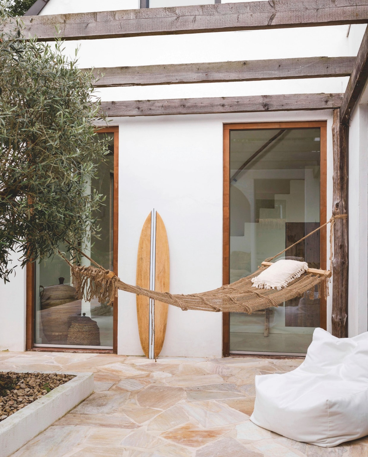 Hangmat, kussen, surfplank en witte loungestoel Coco homeliving. Terrasvloer Van den Heuvel &amp; Van Duuren. vtwonen special zomerboek 12-2025 | fotografie Corine Hoge Bavel-Jansen | tekst Caroline Westdijk