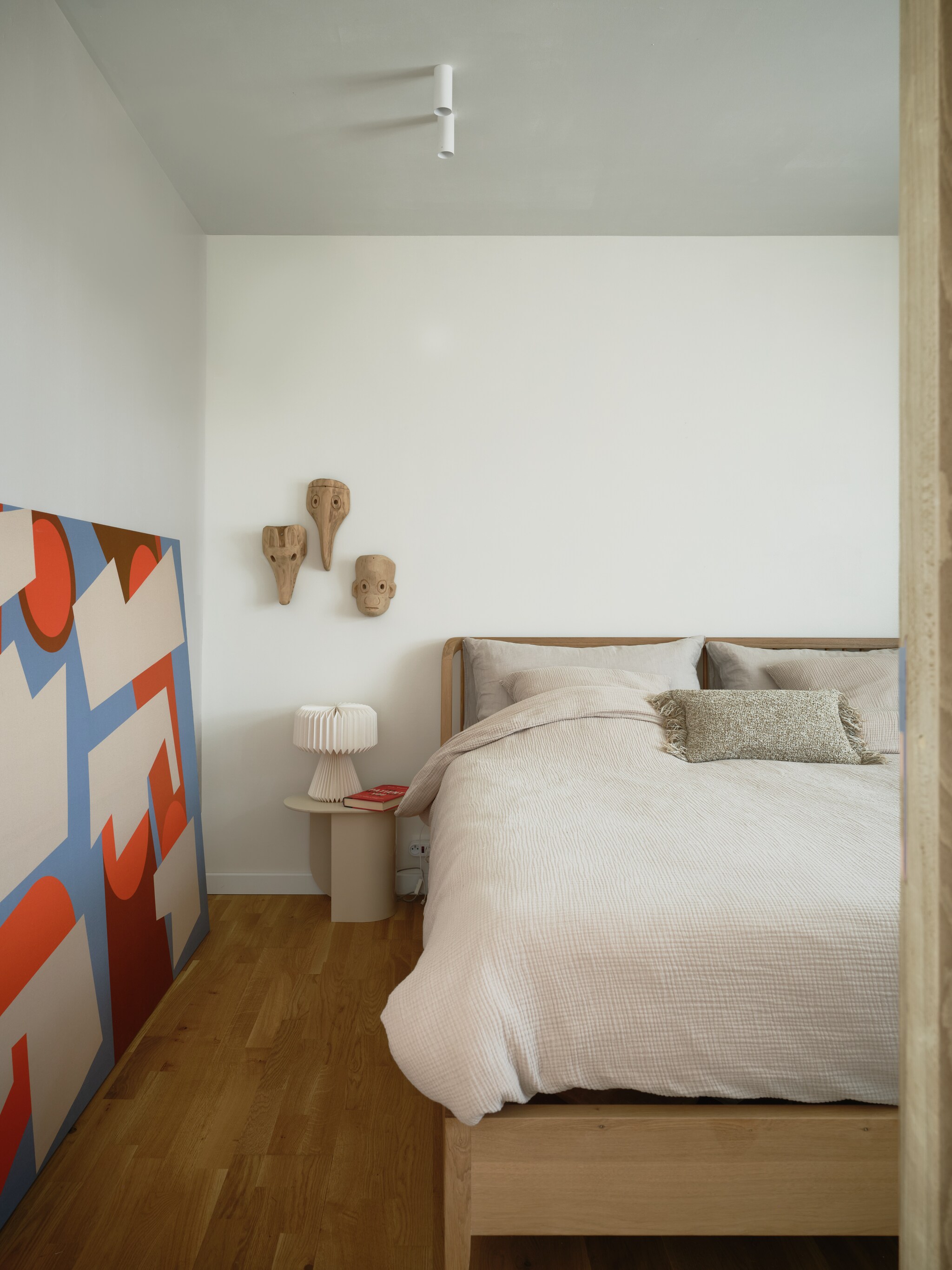 Bed Spindle van Ethnicraft. Nachtkastje Fést.Kunstwerk van Gregory B Studio. Maskers souvenirs uit Guatemala. Beddengoed H&M Home. Spots op maat gemaakt door Cone Lighting. stijlvol wonen 7-2025 | fotografie Mr. Frank
