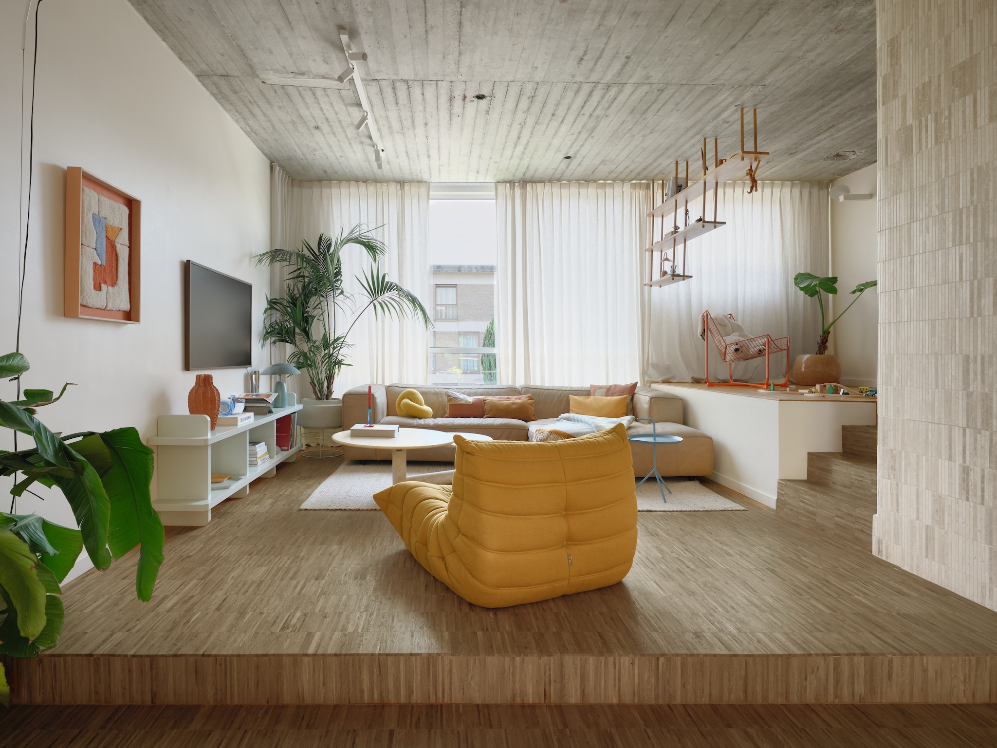 Kunstwerk gemaakt door Camille. Dressoir eigen ontwerp, op maat laten maken door een timmerman. Vintage travertijnen salontafel Roche Bobois. Fauteuil Togo van Ligne Roset. Bank Dunbar van Fést. Bijzettafel DLM van Hay. Hangkast Bond van Fogia. Oranje fauteuil Skalboda van Ikea. Tv The Frame van Samsung. Verlichtingrail op maat gemaakt door Cone Lighting. stijlvol wonen 7-2025 | fotografie Mr. Frank