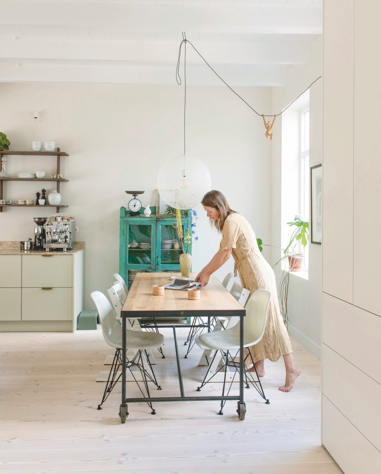 Tafel Barbiers Originals, vaas HKliving, kopjes Atelier van Schaijk, bollamp Moooi, slingeraap Kay Bojesen onder andere te koop via Nordic Nest. Kuipstoelen van Charles en Ray Eames via Bebob Design, kinderstoelen Stokke. Groene kast Van Dijk &amp; Ko, servies erin van oma en kringloopwinkels. Glazen karaf, weegschaal en wit vaasje uit kringloopwinkels. Wanden en ombouwkast rond de voordeur geschilderd in Clay Pale van Little Greene. vtwonen 06-2025 | styling Jeske Weel | fotografie Caroline Coehorst
