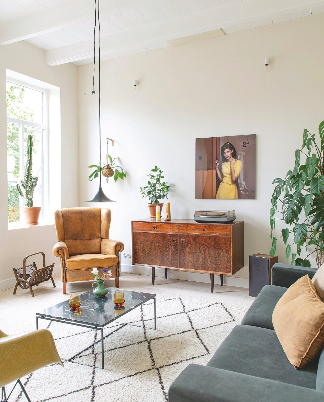 Fauteuil en dressoir Marktplaats, Philips platenspeler van Dicks oma,houten kandelaar Ovo things, foto Erwin Olaf. Hanglamp Semi van Gubi, wandlampen Thpg. Lectuurbak en vaas kringloopwinkel. Bank Torino van Wehkamp. Salontafel Serax, glazen Kwantum, bloemen uit eigen tuin. Vintage fiberglas kuipstoel van Charles en Ray Eames via Bebob Design.Stopcontacten Berker 1930 van Hager, vloerkleed Rozenkelim. vtwonen 06-2025 | styling Jeske Weel | fotografie Caroline Coehorst