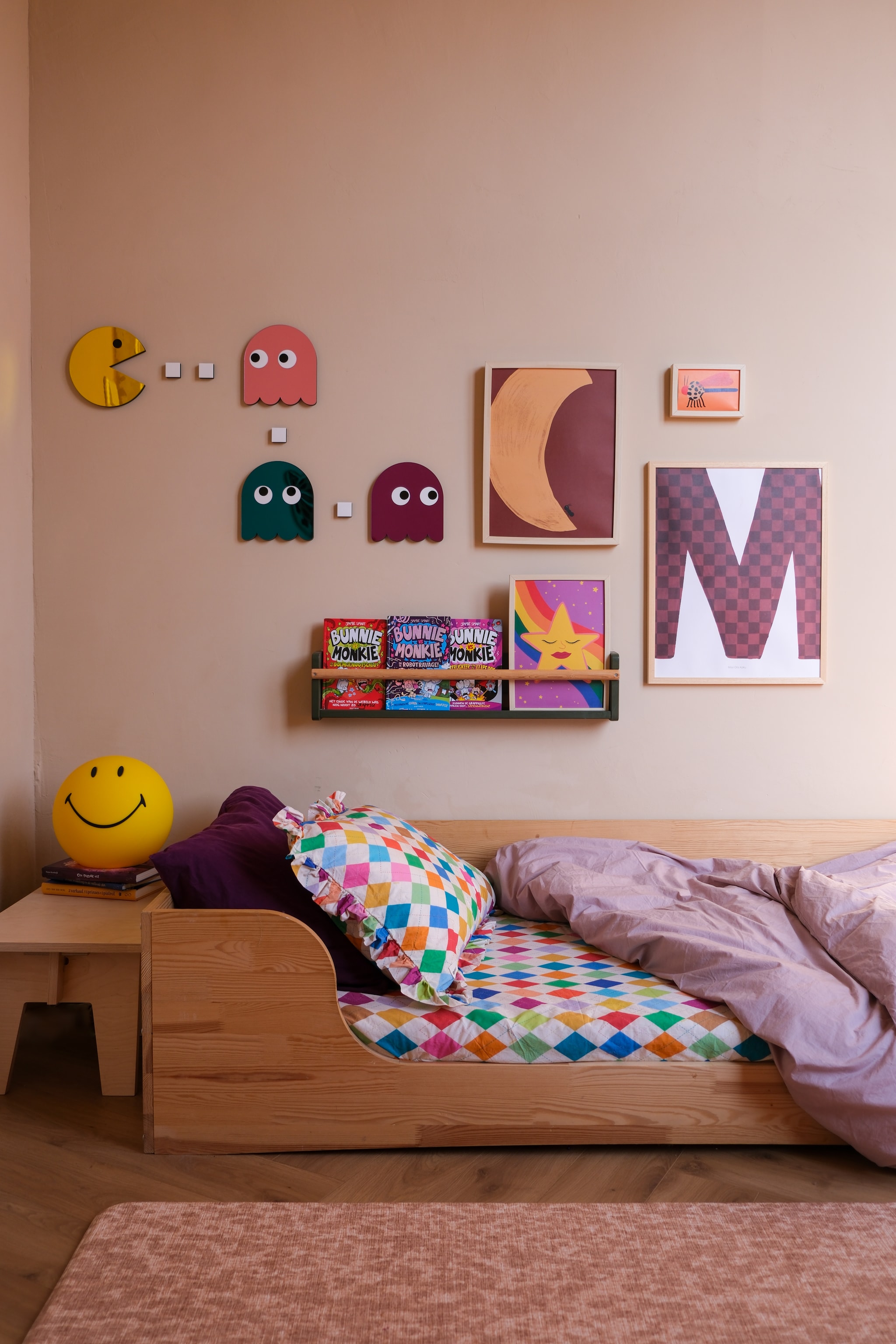 Smiley-lamp Mr Maria, tafeltje Grimms Furniture. Bed Petit Puk, dekbedovertrek La Cerise sur le Gâteau, hoeslaken en kussensloop Mooui Barcelona. Letterposter Mr Starsky, pacman-spiegels La Miséto, maanposter Studio by Diede x Aniek Bartels, kaart met libelle Aniek Bartels, poster met ster Jungle Mumble Design. Geschilderd boekenrek Ikea. Speelmat Totter+Tumble. Vloer laminaat visgraat Peterselie van Douwes Dekker. Muurverf Saint-Tropez van Lab Paint. fotografie Rio van der Oest @mostlymosi