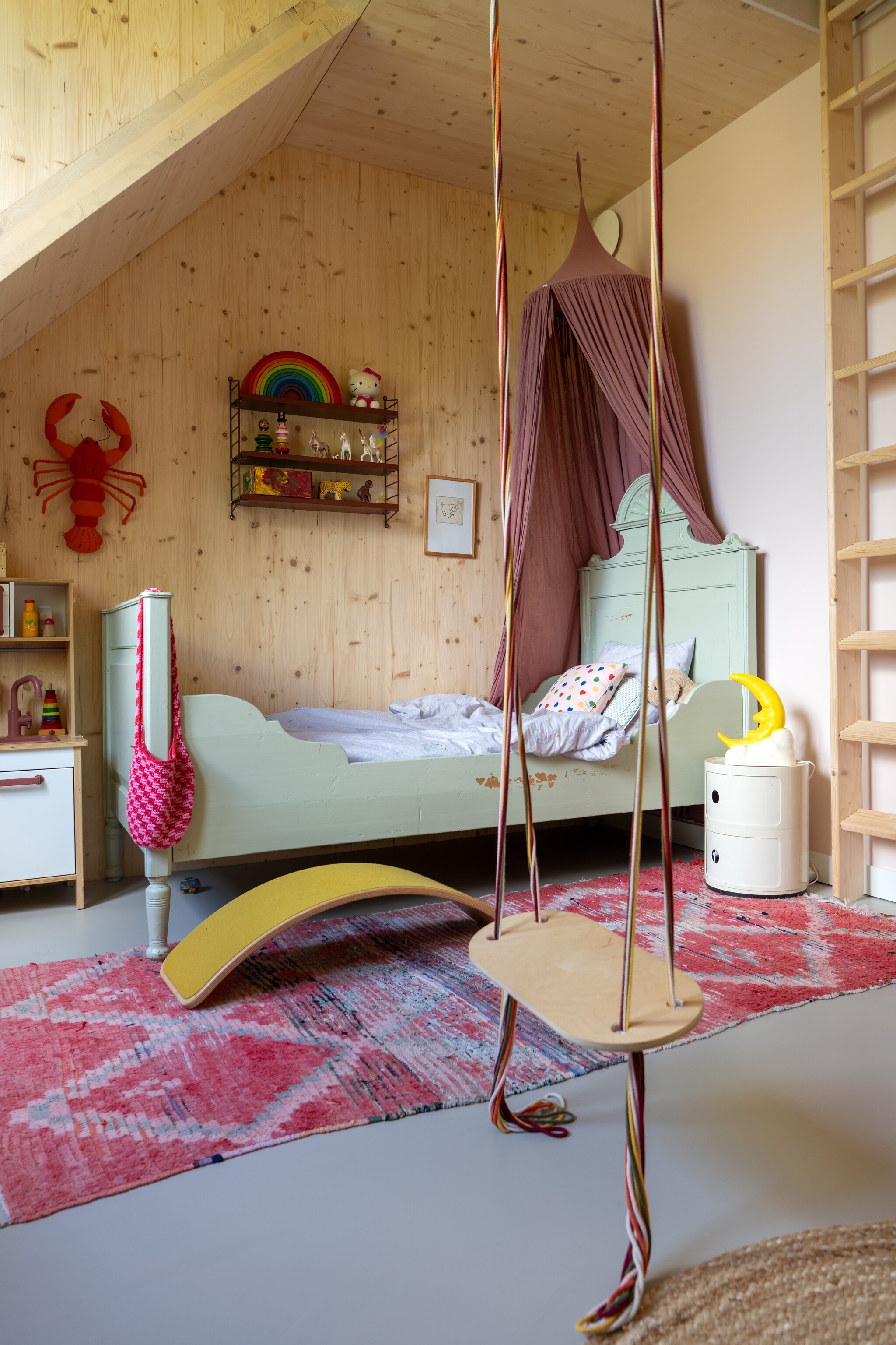 Bed vintage via Marktplaats, hemel Numero 74. Vloerkleed The Souks, nachtkastje Kartell. Gele boog Wobbel, schommel Babai Toys. Kreeft Fiona Walker, nachtlampje kringloop. Muurkleur Pink Groundvan Farrow & Ball. vtwonen 09-2025 | styling Jasmijn Stegeman | fotografie Anke Leunissen