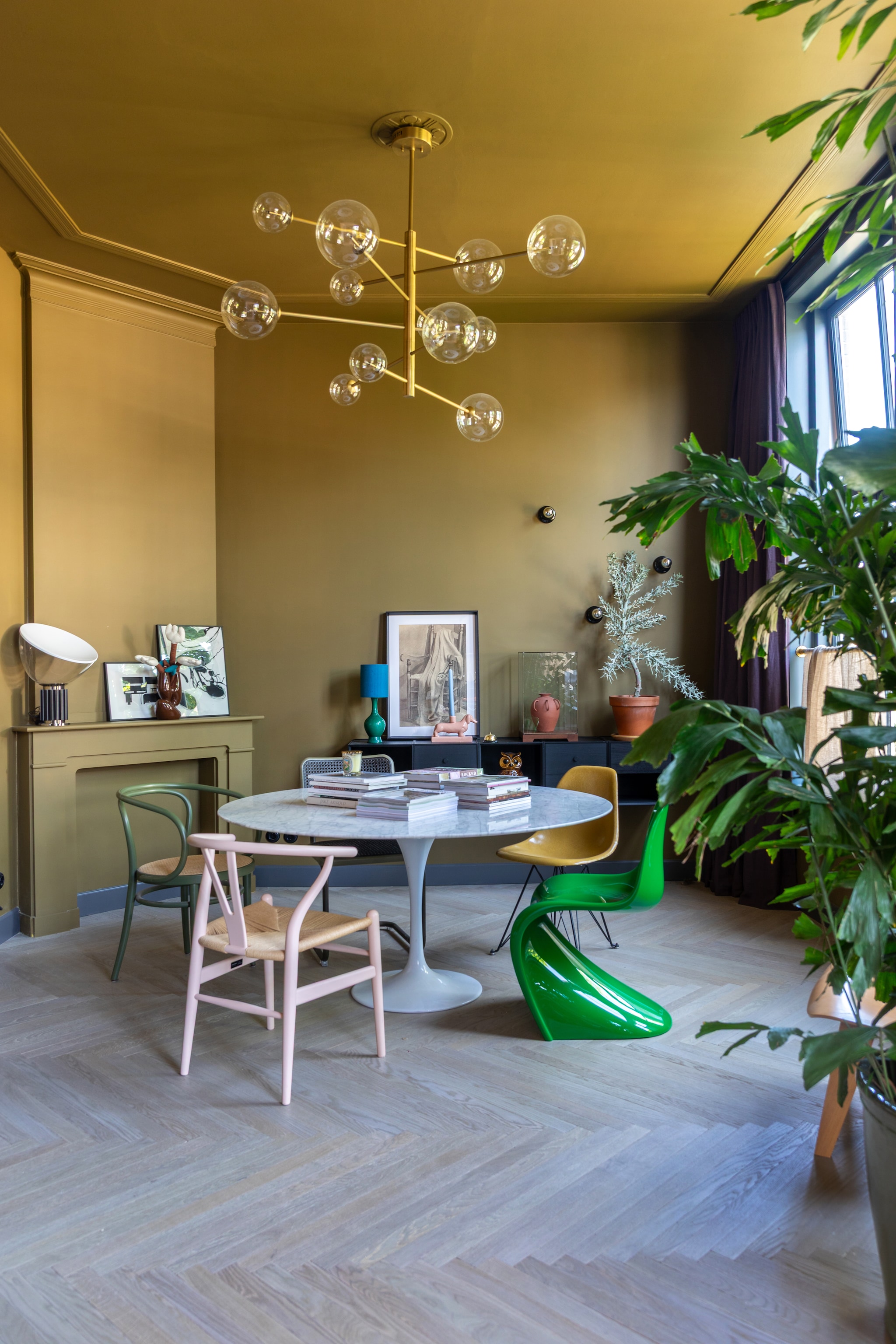 Kleur muren en plafond The Greenhouse 7 van Flexa, houten vloer Vloerenhuis Amsterdam. Eettafel Knoll, stoel links Carl Hansen Pink Limited via Mister Design, groene stoel Vitra. Kunstwerk links Werk aan de Muur, kunstwerk rechts gemaakt door Theo-Berts opa. Tafellamp op schouw Flos. Dressoir Audo, kaarsenhouder teckel Theo-Bert Pot by Karwei. vtwonen binnenkijken 09-2025 | styling en fotografie Theo Bert-Pot, Jelle van de Schoor