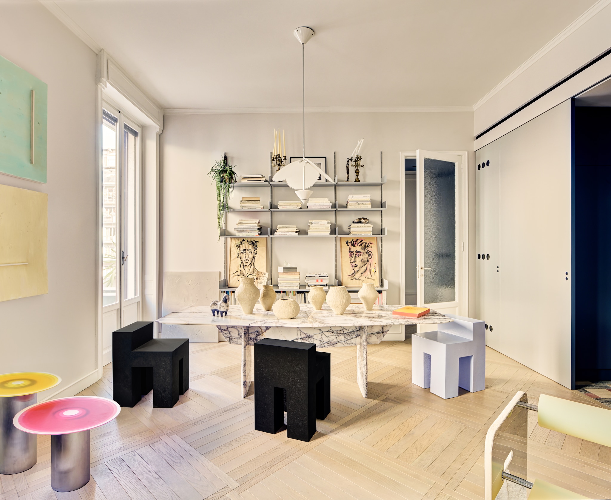 Bijzettafels, schilderijen en tafel Elmaz van Rudy Faissal. Lila en zwarte stoelen Finemateria. Vazen Amoraw Studio. Wandplanken Vitsoe. Portretten Alessandro Mannelli. Hanglamp Artemide.   Stijlvol Wonen 6-2025 I Productie Living Inside | Styling Giulia Taglialatela I Fotografie Mattia Iotti