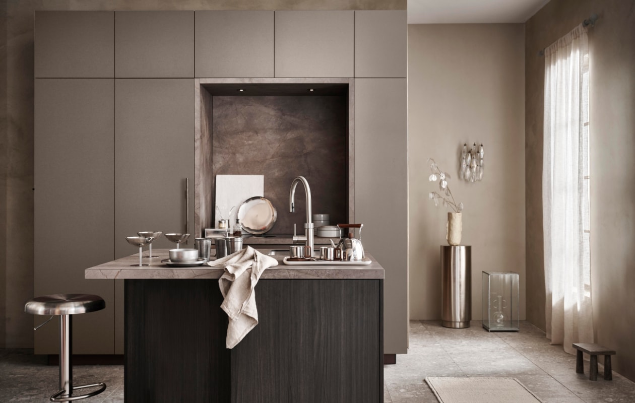 vtwonen keuken Tricolore, kwartsietgrijs, in deze opstelling € 23.500,-.

M.m.v. shop.vtwonen.nl (vloertegel Composite donkergrijs), basiclabel.nl (barkruk Isaac), hetkabinet.nl (marmeren snijplank, rond schilderbord, tak met zilveren blaadjes, metalen vitrinebox, glazen vaas, beige vaas op pilaar), zarahome.com (gordijnen, travertin kruk, vloerkleed, stalen mok met acaciahouten schotel, stalen theepot met acaciahouten details, metalen wijnglazen, glazen slabestek), instagram.com/theartoflumi (glazen wandlamp), thefinestore.com (By Mölle theedoek Pinstripe Flax, Redecker metalen opbergbox, Ferm Living rvs kom, bord en bekers Tumbled, Hasami grijs porselein servies, kommen en borden, Fog Linen Work dienblad Linen Tray Natural). Privébezit (pilaar). vtwonen 07-2025 | styling Kim van Rossenberg | fotografie Sjoerd Eickmans