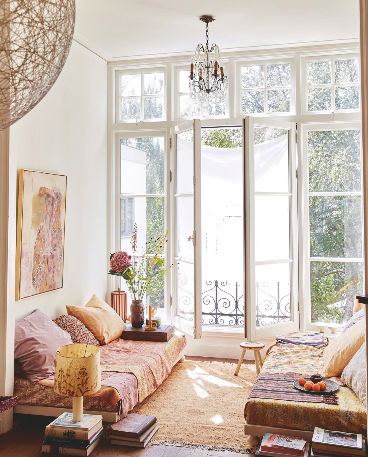 Banken eigen ontwerp. Hanglamp Random Light van Bertjan Pot via Moooi. Kroonluchter Nuzzelspul. Kussens zelfgemaakt. Kleden uit India, Marokko en Indonesië (ikat). Schilderskist als tafel erfstuk. Vazen, kruk en lamp op boeken  rommelmarkten. Vloerkleed Liv Interior. Schilderij tinystories. vtwonen 7-2025 | styling Marianne Luning | fotografie Tjitske van Leeuwen