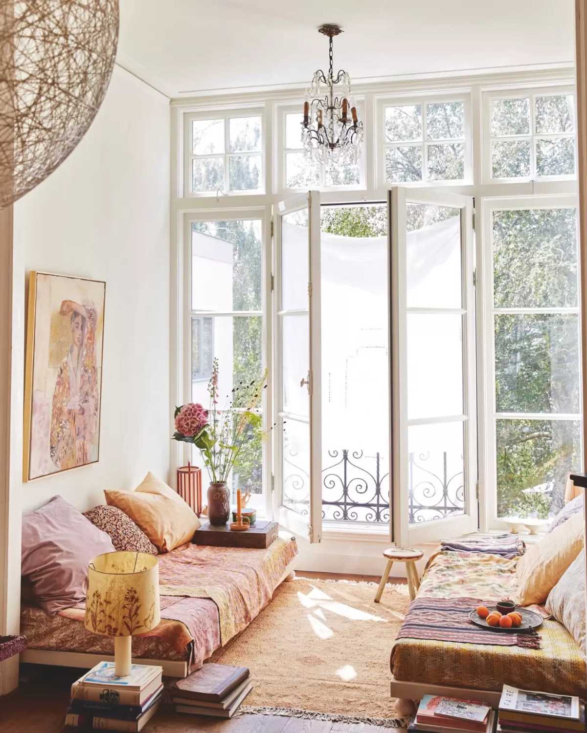 Banken eigen ontwerp. Hanglamp Random Light van Bertjan Pot via Moooi. Kroonluchter Nuzzelspul. Kussens zelfgemaakt. Kleden uit India, Marokko en Indonesië (ikat). Schilderskist als tafel erfstuk. Vazen, kruk en lamp op boeken  rommelmarkten. Vloerkleed Liv Interior. Schilderij tinystories. vtwonen 7-2025 | styling Marianne Luning | fotografie Tjitske van Leeuwen