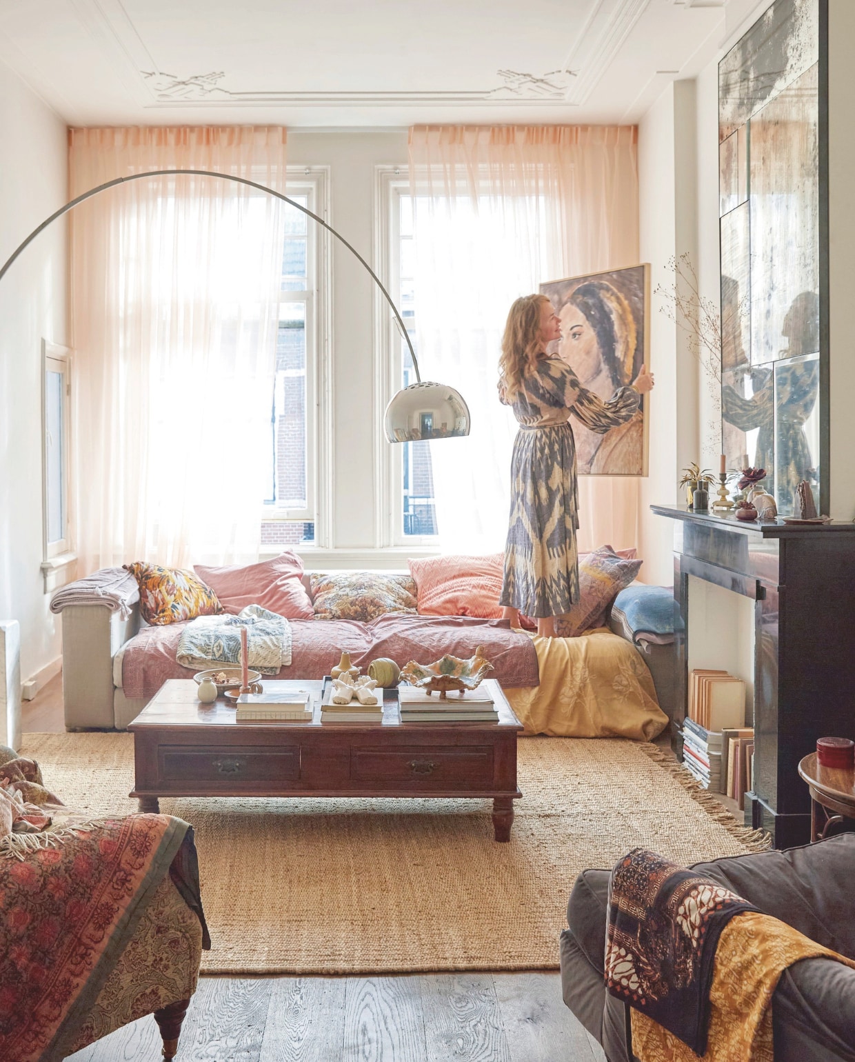 Vloer antiek donker eiken. Muurverf ral 9010. Gordijnen in blush van stoffenmarkt Utrecht. Bank, salontafel en stoelen tweedehands. Vloerkleed HKliving. Lamp Flos Arco. Kussens zelfgemaakt, Van Verre en The Souks. Spiegel op maat gemaakt door Piet Jonker. Schilderij Berber Girl tinystories. Stoffen meegenomen van reizen. vtwonen 7-2025 | styling Marianne Luning | fotografie Tjitske van Leeuwen