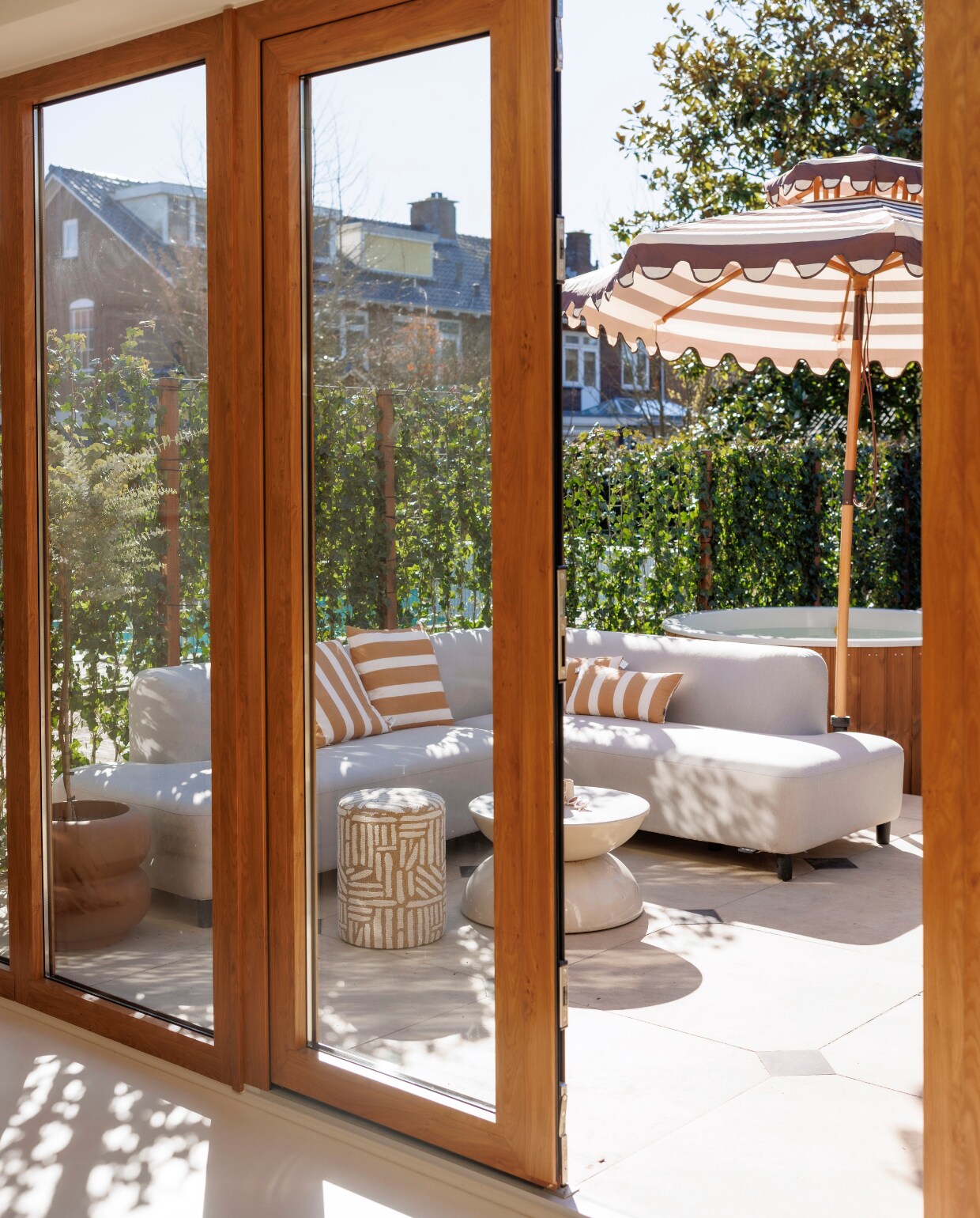 Tegels terras restpartij. Zwarte tegels Jan van IJken Oude Bouwmaterialen. Verwarmde buitenbank en gestreepte kussens Hartman. Salontafel Westwing. Poef Amstelièr. Plantenpot Elho. Parasol HKliving. Hottub Welvaere.  vtwonen 7-2025 | fotografie Emma Peijnenburg