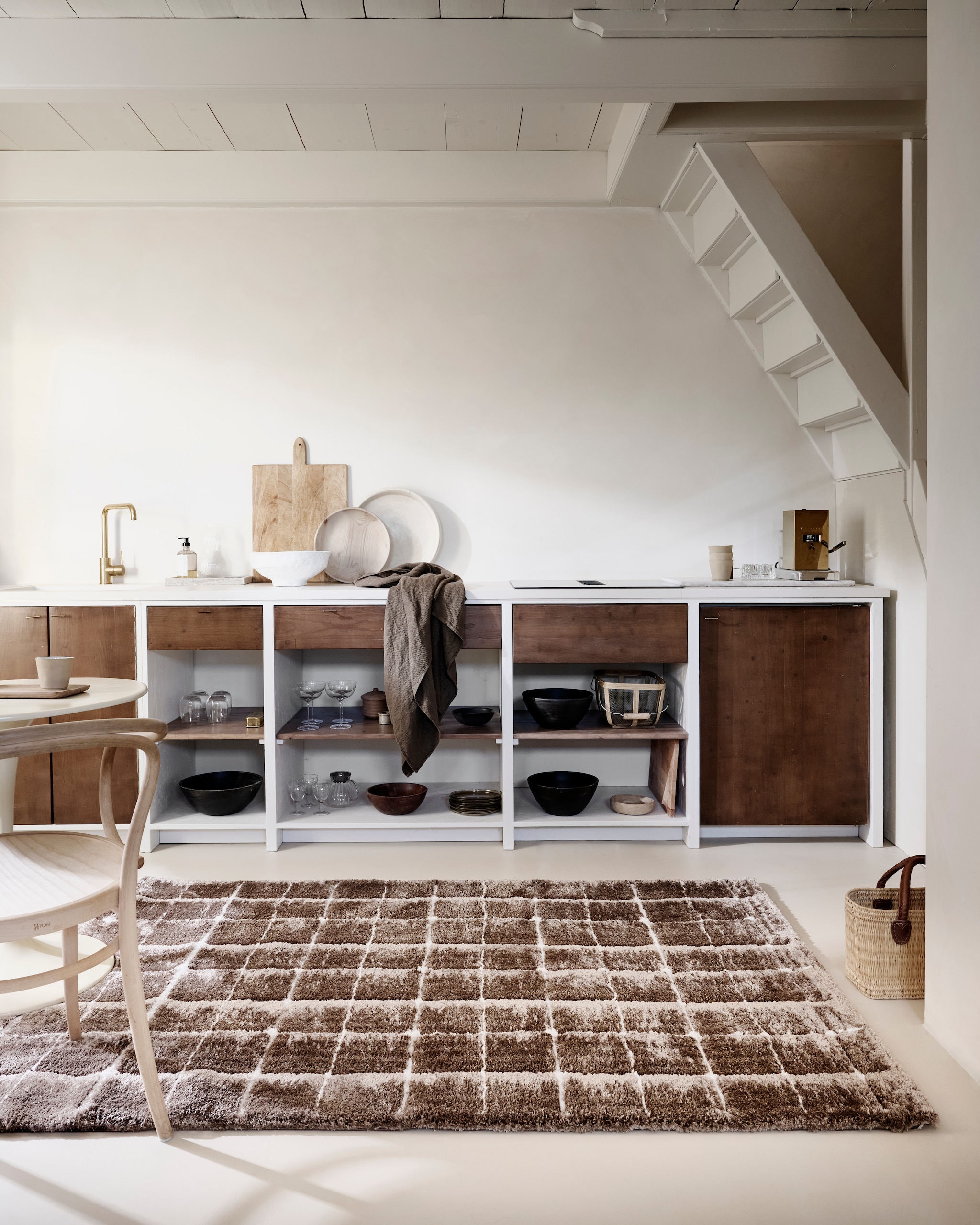 vtwonen vloerkleed Blocks, gerecycled polyester en jute, warm brown, vanaf 80x240 cm € 239,-.M.m.v. dille-kamille.nl (stoel, houten schalen, tadelakt schaal, rieten tas, tafel), householdhardware.nl (glaswerk, linnen doek, oogstmand, kruk), letoile.store (zeepdispenser). vtwonen 10-2025 | styling Sanne Ketelaar, Marlies Does | fotografie Sjoerd Eickmans, Peggy Janssen