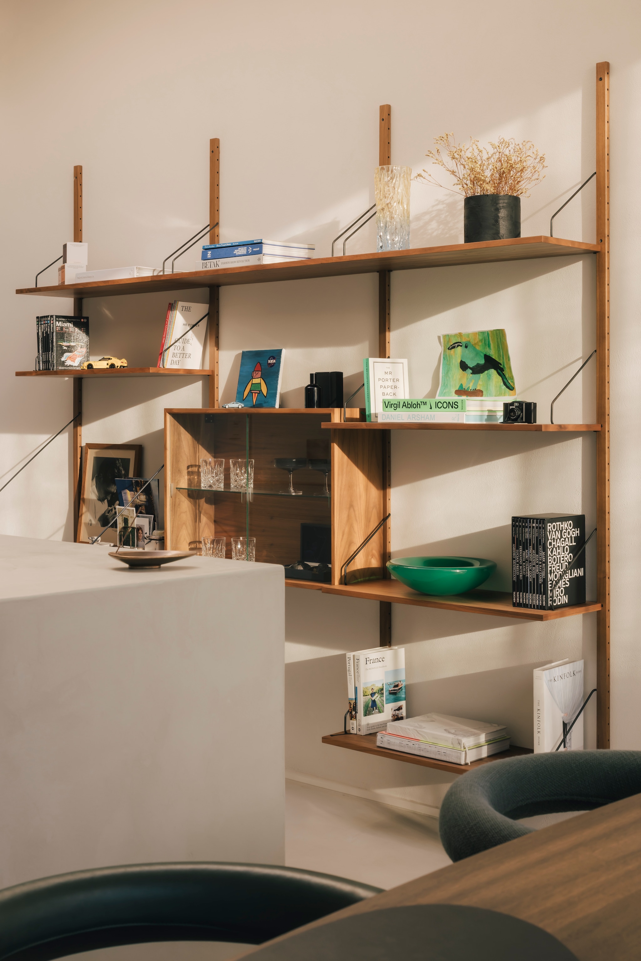 Het modulaire wandsysteem van Royal System vulde Nachtergaele met persoonlijke items, waaronder boeken en internationale magazines over kunst, design en reizen. De groene resin schaal is een ontwerp van Vincent de Rijk voor Rira Objects. Stijlvol wonen 9-2025 | Katoo Peeters