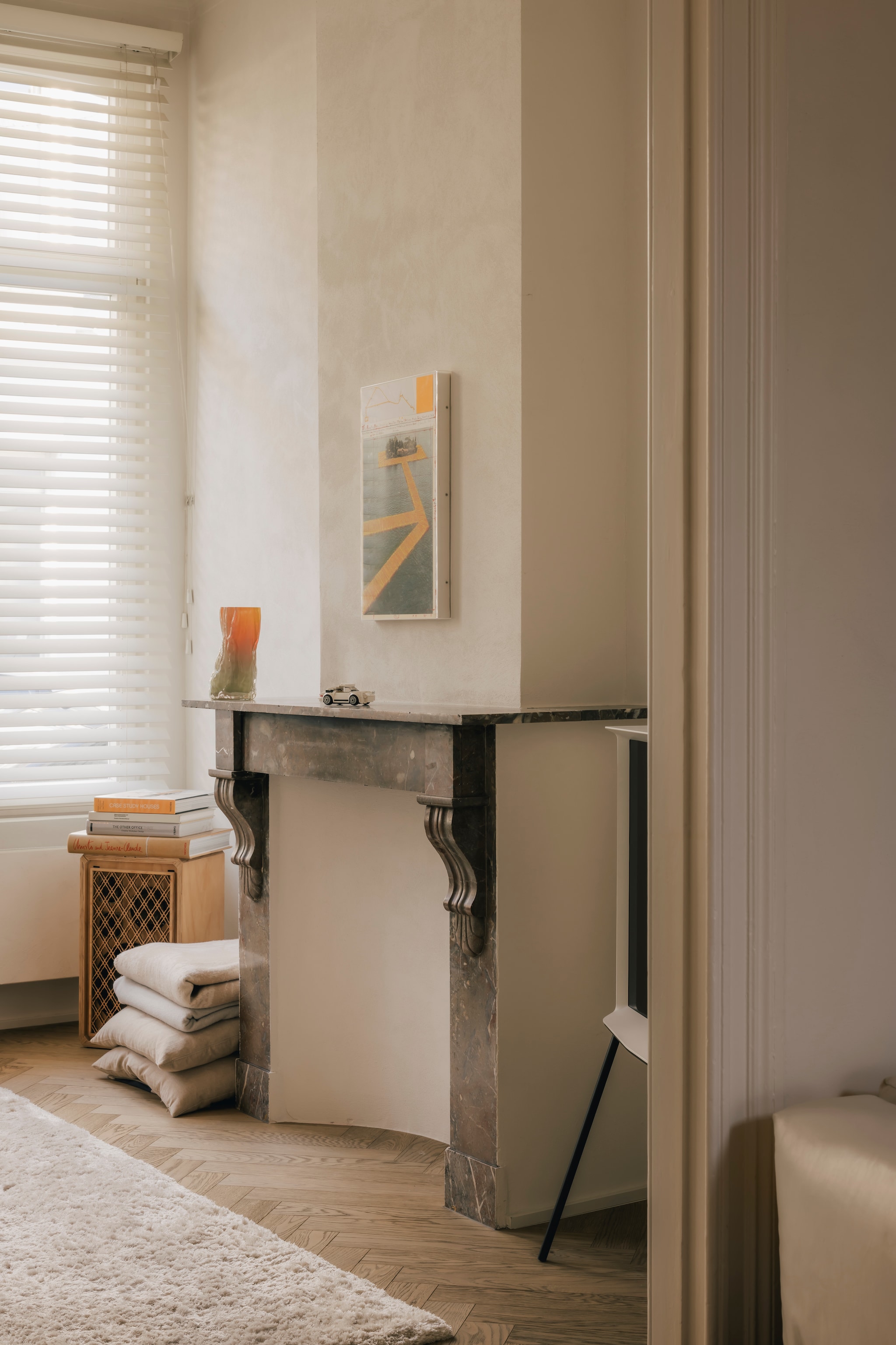 Boven de originele schouw met marmeren elementen hangt een ingelijste lithografie van kunstproject The Floating Piers, dat de Bulgaarse kunstenaar Christo in 2016 bij het Iseomeer bewerkstelligde. Stijlvol wonen 9-2025 | Katoo Peeters