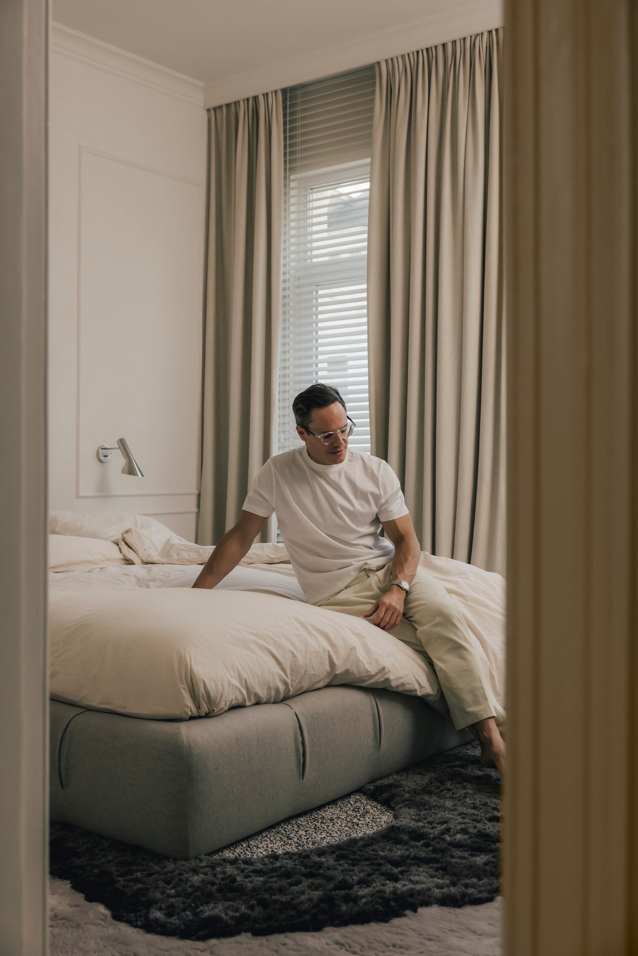 In de slaapkamer werden beige tinten als basis gebruikt. Het vloerkleed komt uit een samenwerking van de Belgische tapijtenfabrikant JOV met Studiopepe. Aluminium wandlamp, AJ 50 van Louis Poulsen. Stijlvol wonen 9-2025 | Katoo Peeters