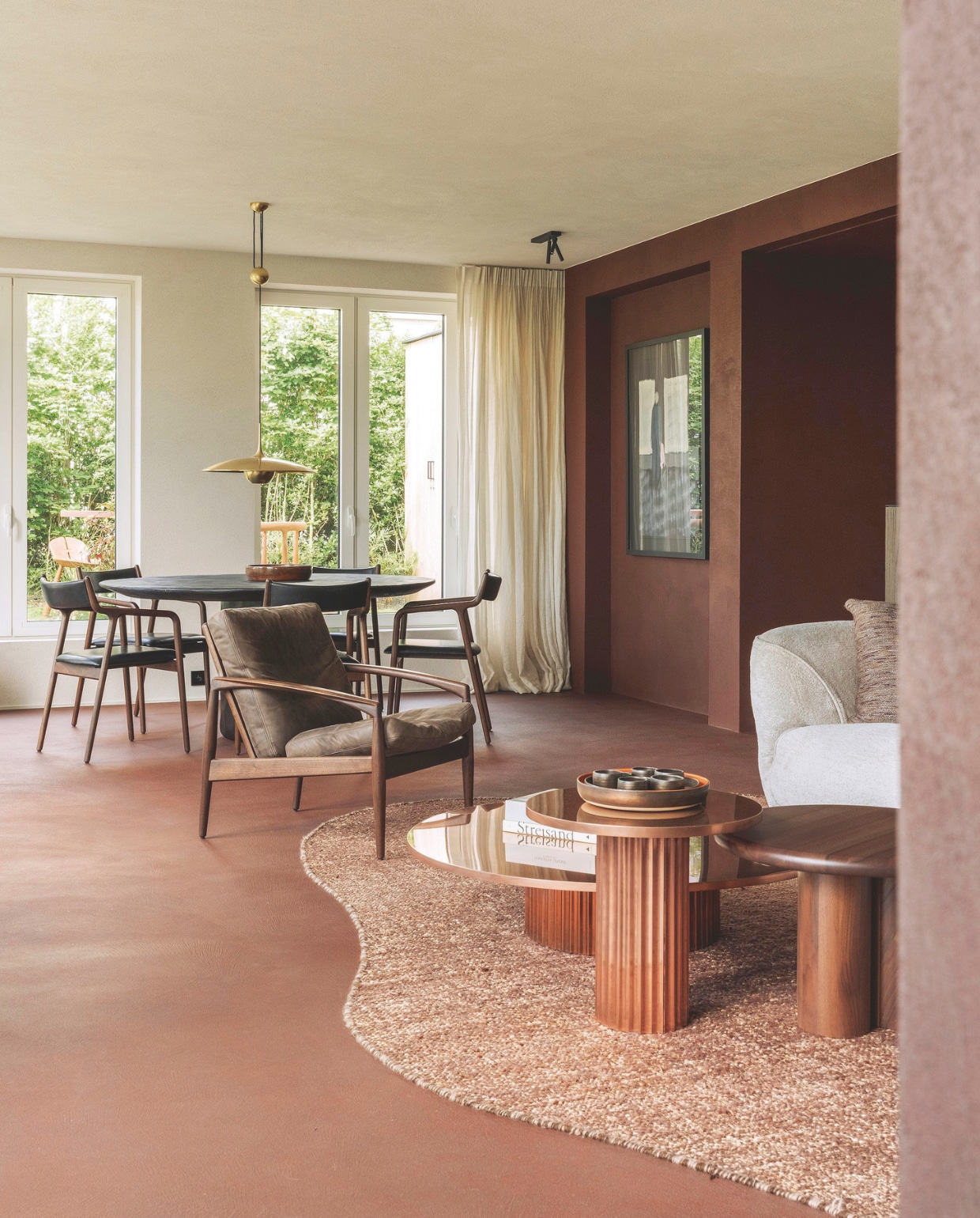 Binnen is gekozen voor diepe, warme roodtinten, naar buiten toe geven de lichte muren, plafonds en gordijnen een luchtige touch. Fauteuil Paperknife van Miyazaki. Eettafel Benoit Viaene. Lamp Onos 55 van Florian Schulz.  stijlvol wonen 7-2025 | fotografie Tijs Vervecken