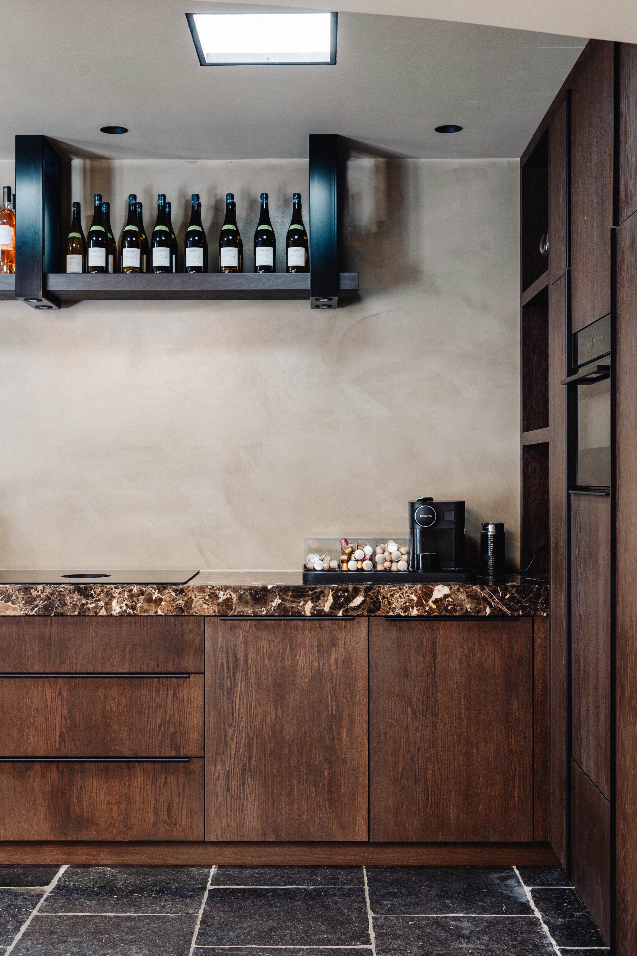 Het wijnrek in de keuken van de werkruimte is op maat gemaakt van donker hout en steekt mooi af tegen de wand van beton ciré. Stijlvol Wonen 9-2025 | fotografie Stie de Neve