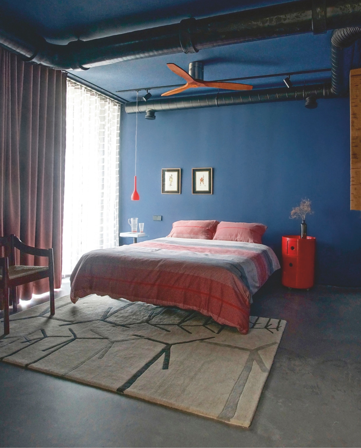 Het nachtkastje is van Kartell, de hanglamp is vintage. De buizen van de ventilatie-unit werden zwart geschilderd zodat ze optisch wegvallen. Stijlvol Wonen 8-2025 | Styling & Fotografie Bart Wigger | Tekst Evelien Roels