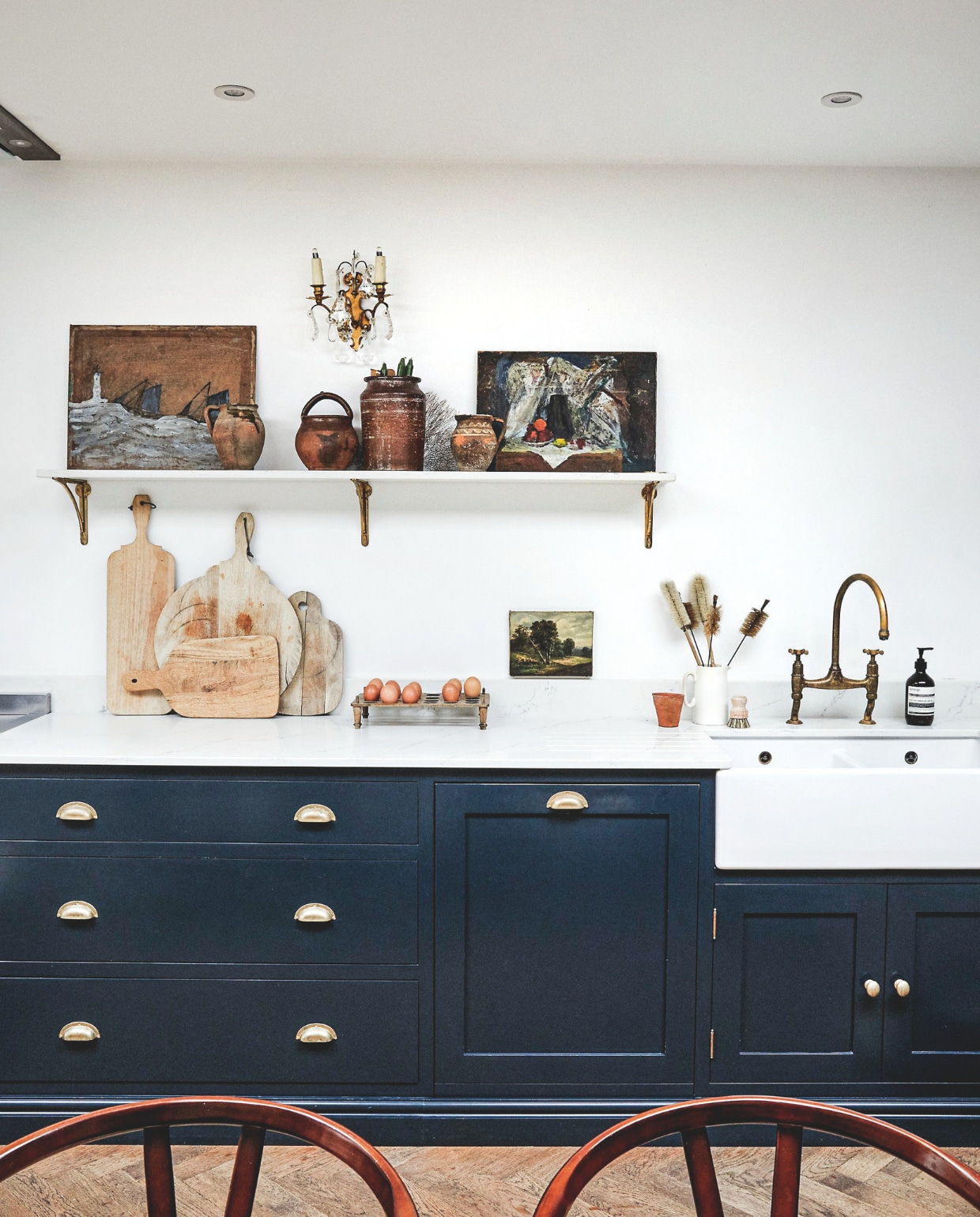 Keuken Evie Willow. Kastfronten in Black Blue van Farrow & Ball. Kraan Devol. Snijplanken, ornamenten en schilderijtjes Article 3 Interiors. Kleinste schilderij erfstuk van Caitlins moeder. Wandlamp Station Mill Antiques. Muurverf Brilliant White van Dulux. vtwonen Landelijk 9-2025 | fotografie Brent Darby | tekstbewerking Anneleen Peeters