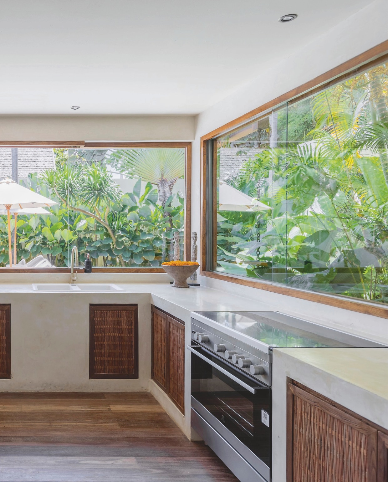 De keuken werd minimalistisch gehouden om alle aandacht naar buiten te laten gaan. De tuin met tropische planten wordt visueel naar binnen gehaald door de grote raampartijen. vtwonen Landelijk 8-2025 | fotografie Sheila Man | tekstbewerking Marie Masureel