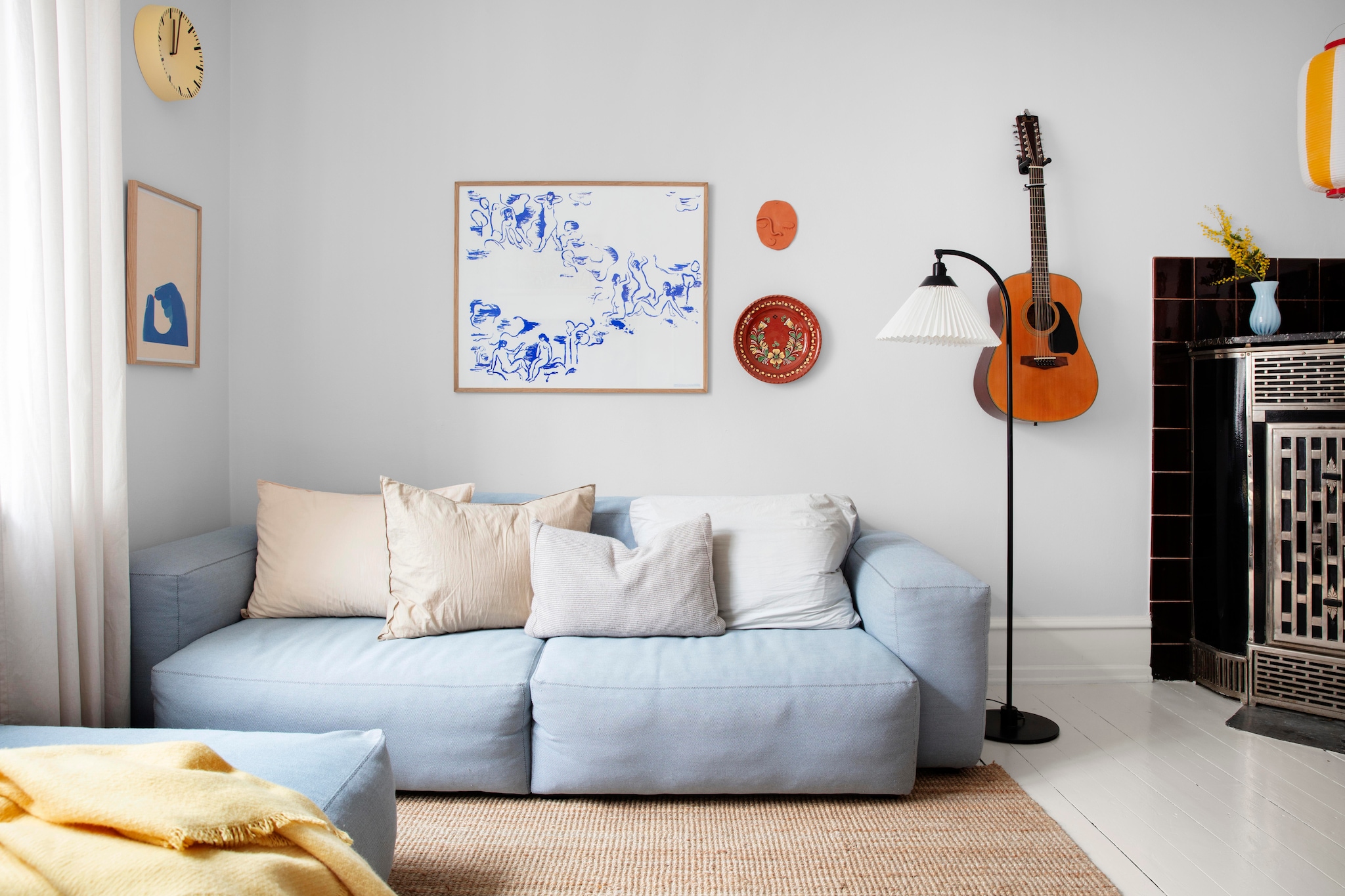 Bank, plaid en klok Hay. Kussens Aiayu. Ingelijst behang ontwerp van Poul Henningsen. Keramieken object  gezicht Emma Louise Gram Heegaard. Bord rommelmarkt. Vloerlamp Le Klint. Hanglamp cadeau gekregen uit Japan. Vloerkleed en gordijnen Ikea. Gitaar Ibanez. vtwonen 01-2026 | productie Living Inside | styling Rikke Graff Juel | fotografie Christina Kayser O.