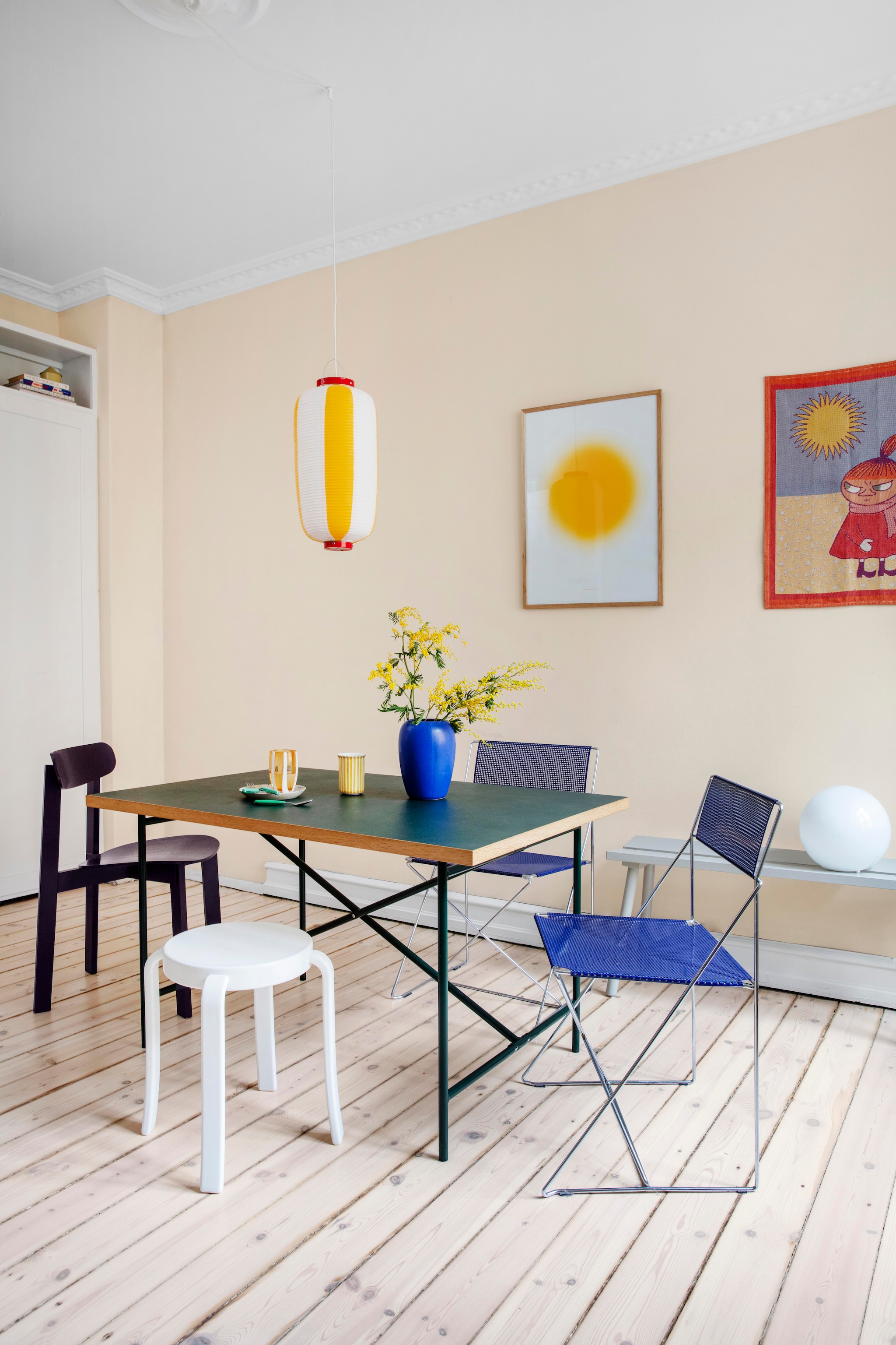 Eettafel van Egon Eiermann. Stoelen X-line van Niels Jørgen Haugesen. Auberginekleurige stoel Please wait to be seated. Kruk 8000 van Magnus Olesen. Hanglamp cadeau gekregen uit Japan. Vintage vaas Holmegaard. Beker erfstuk van Amalie’s oma. Glas Zafferano Italia. Poster Ace & tate X Playtype. Illustratie Little my van Tove Jansson. vtwonen 01-2026 | productie Living Inside | styling Rikke Graff Juel | fotografie Christina Kayser O.