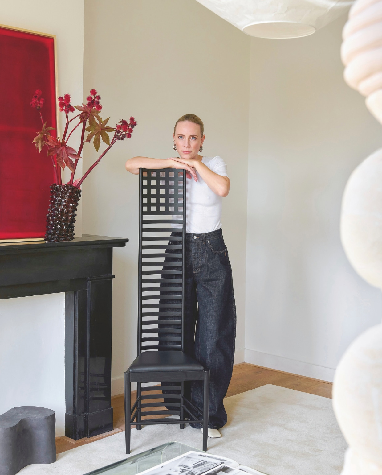 Gloria draagt een T-shirt van Ganni. Jeans Jacquemus. Schoenen Wandler. Oorbellen Panconesi. Stoel Hill House 1 van Cassina, ontwerp Mackintosh. Stijlvol wonen 9-2025 | styling Marianne Luning | fotografie Kasia Gatkowska | modestyling Tamara Botter |  tekst Anneleen Peeters | Visagie Victoria Osborn