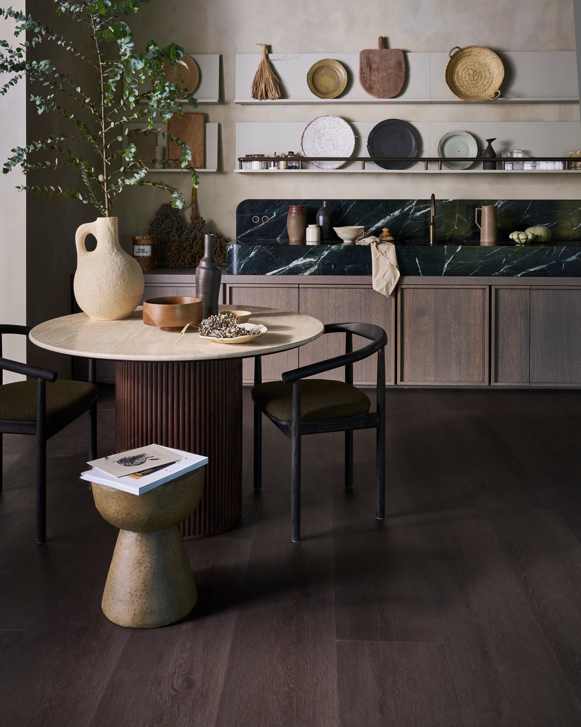 vtwonen pvc-vloer Wide Board, charcoal, 152,5x30,5 cm, dryback per m² € 44,95, click per m² € 57,95.M.m.v. dutchbone.com (eettafel Arda), urbannatureculture.com (witte vaas), marjokedeheer.com (keramieken borden, schalen, flessen), @nel_punt (houten schalen). Overig privébezit. vtwonen 01-2026 | styling Cleo Scheulderman | fotografie Jeroen van der Spek