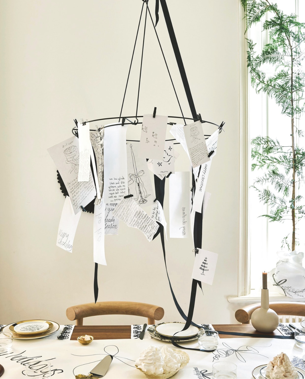 vtwonen decoratiering, metaal, zwart en goud, 60 cm (Ø) € 29,95, kandelaar, metaal, flax € 16,95, borden, porselein, wit-goud, set van 2 € 25,-, of als serviesset 16-delig € 167,20, petitfourborden, porselein, goud, set van 4 € 24,95, bestekset, staal, matzwart, 18-delig € 89,- (shop.vtwonen.nl). Studio Henk eetkamerstoel Checker, eiken, naturel light, 54,5x53,5x79,5 cm (bxdxh) € 929,- en eettafel Soft, eiken, walnoot naturel, 220x90 cm (lxb) vanaf € 2059,- (studio-henk.nl). Arket tafelloper, katoen € 29,- en geïllustreerd bord Café, porselein € 10,- (arket.com). Overig privébezit. vtwonen special Kerstboek 2025 | styling Sanne Ketelaar | fotografie Alexander van Berge