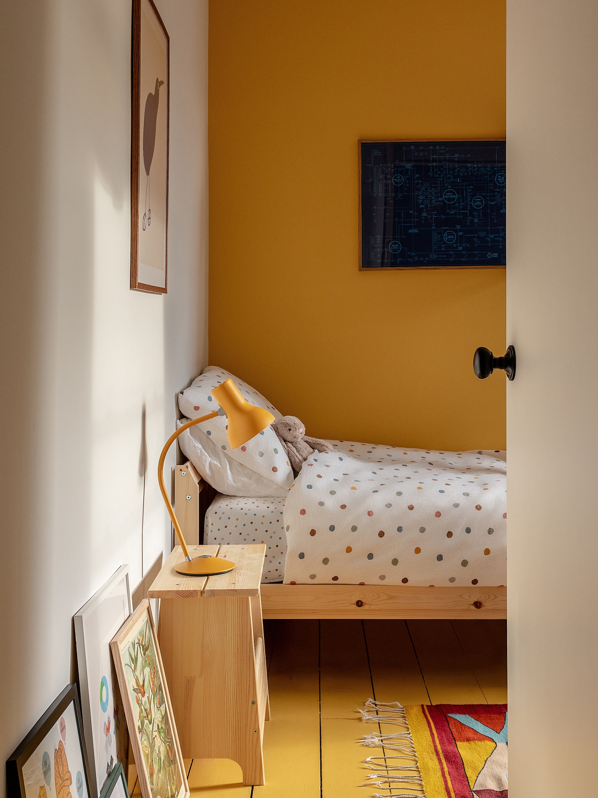 Muurkleur Yellow 03 van Lick. Bed en nachtkastje Ikea. Beddengoed H&m Home. Vloerkleed souvenir uit Mexico. Schilderij aan de wand Dorothy. Staande lamp Type 75 Mini van Anglepoise. vtwonen 02-2026 | fotografie Taran Wilkhu |  productie Living Inside