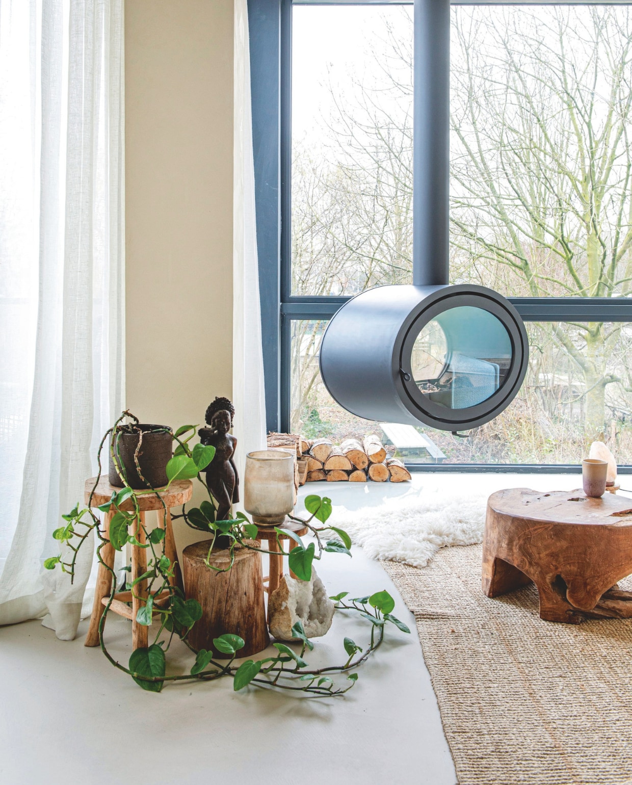 Kruk, houtblok, schapenvacht, beeld kringloop. Windlicht en zoutlamp Fabula Rosa. Houtkachel Dik Geurts. Salontafel kringloop. Gordijnen Elle La. Mok Bolia. Juten vloerkleden La Redoute. vtwonen 12-2025 | styling Annemieke Paarlberg | fotografie Caroline Coehorst | tekst Ina Babbé