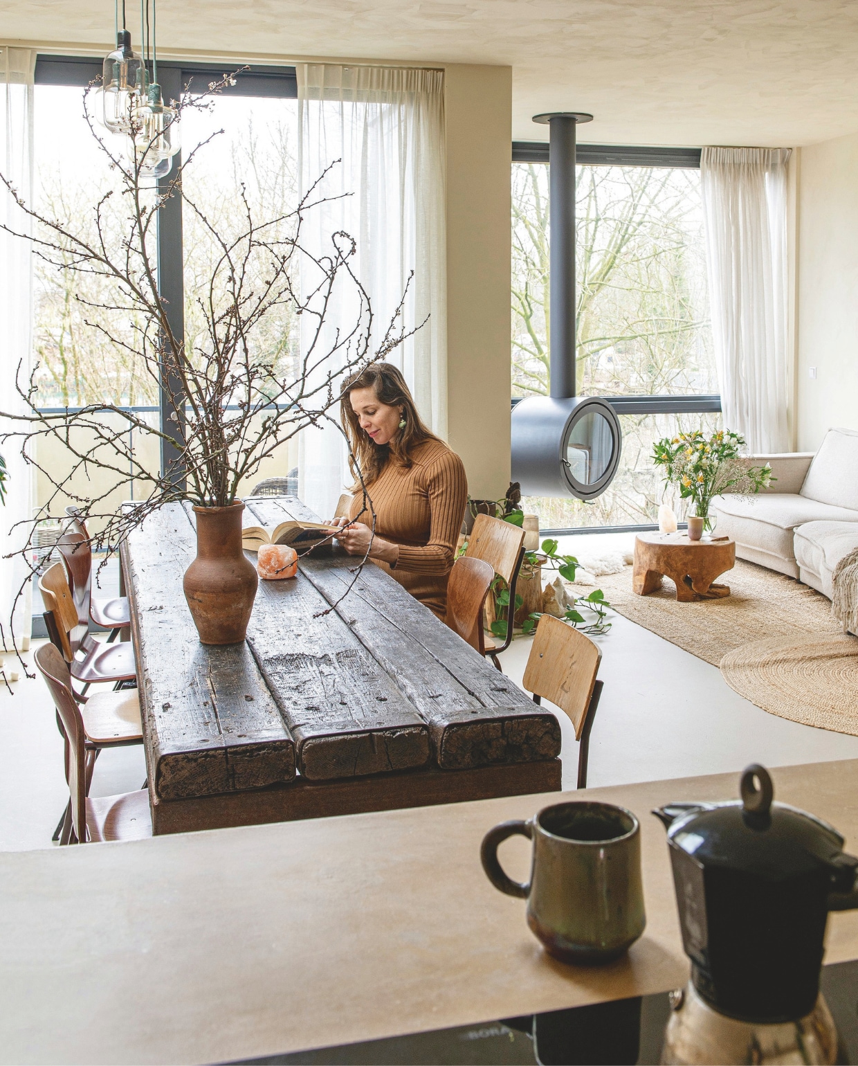 Verf wanden en plafond Mykonos van We Are Wow Makers. Vloer van klei van Creative Plasters. Eettafel, stoelen, salontafel kringloop. Bank Bolia. Gordijnen Elle La. Jute vloerkleden La Redoute. Houtkachel Dik Geurts. Lampen boven eettafel Sklum. Oude vaas op tafel Burbri Antiek. Rieten lampen Uma Cantik. Percolator Bialetti. Mok uit een atelier in Egypte. vtwonen 12-2025 | styling Annemieke Paarlberg | fotografie Caroline Coehorst | tekst Ina Babbé