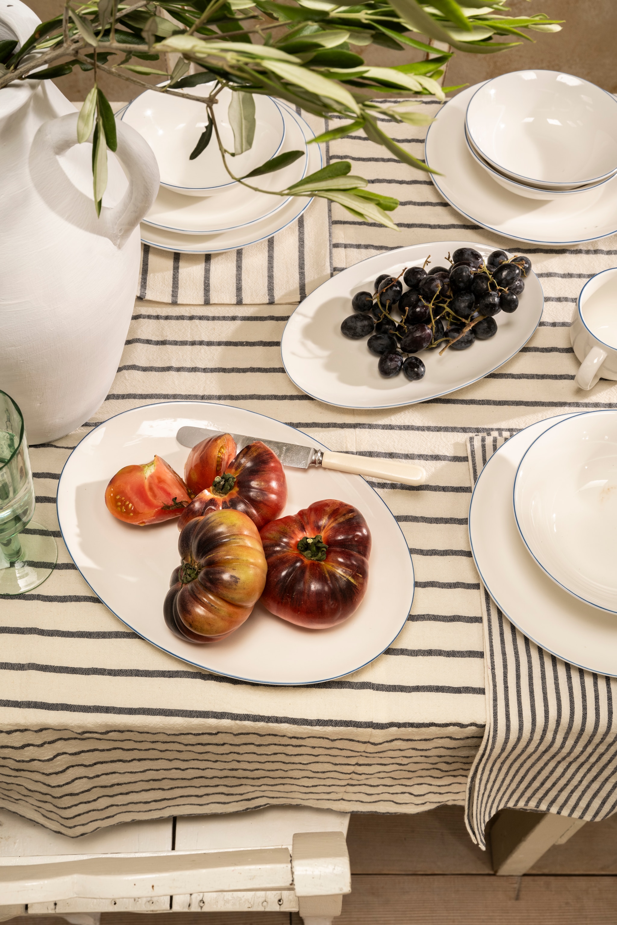 vtwonen tafelkleed, katoen en linnen, blauw en wit, 150x250 cm (lxb) € 79,95, vtwonen servetten, katoen en linnen, blauw en wit, 40x40 cm (lxb), set van 2 € 15,95, vtwonen servetten, katoen en linnen, naturel en grijs, 40x40 cm (lxb), set van 2 € 9,50, vtwonen bord porselein, wit en blauw, diverse maten, vanaf € 9,50, vtwonen pastabord, porselein, wit en blauw, 25,5 cm (Ø) € 17,95. vtwonen 04-2026 | styling Sanne Ketelaar | fotografie Stan Koolen