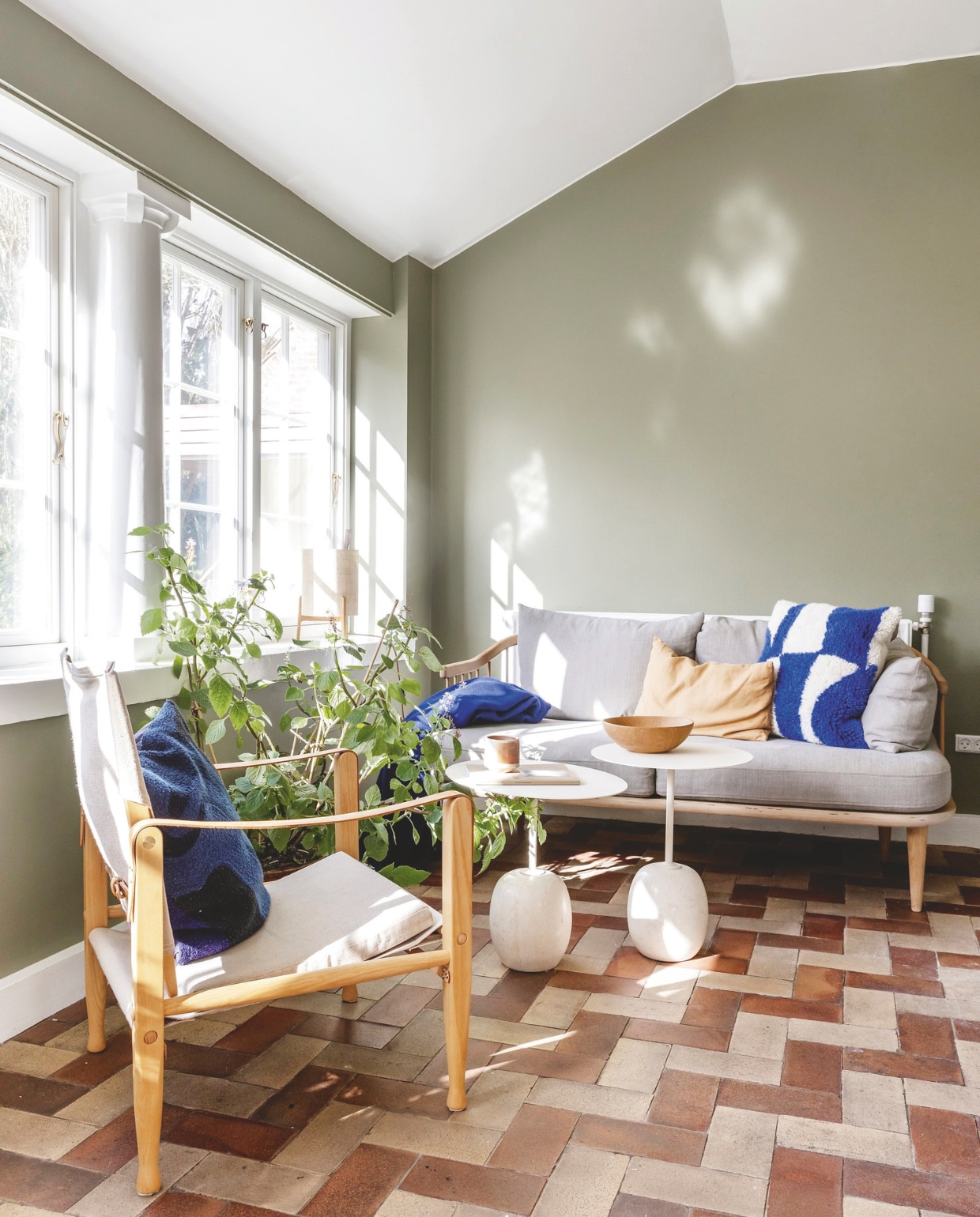 Muurkleur Green Harmony van Jotun, vergelijkbare tint Mild Tundra van Flexa. Originele terracotta tegels. Fauteuil Safari van Kaare Klint. Bank en bijzettafels &Tradition. vtwonen 02-2026 | styling Rikke Graff Juel | fotografie Christina Kayser O.
