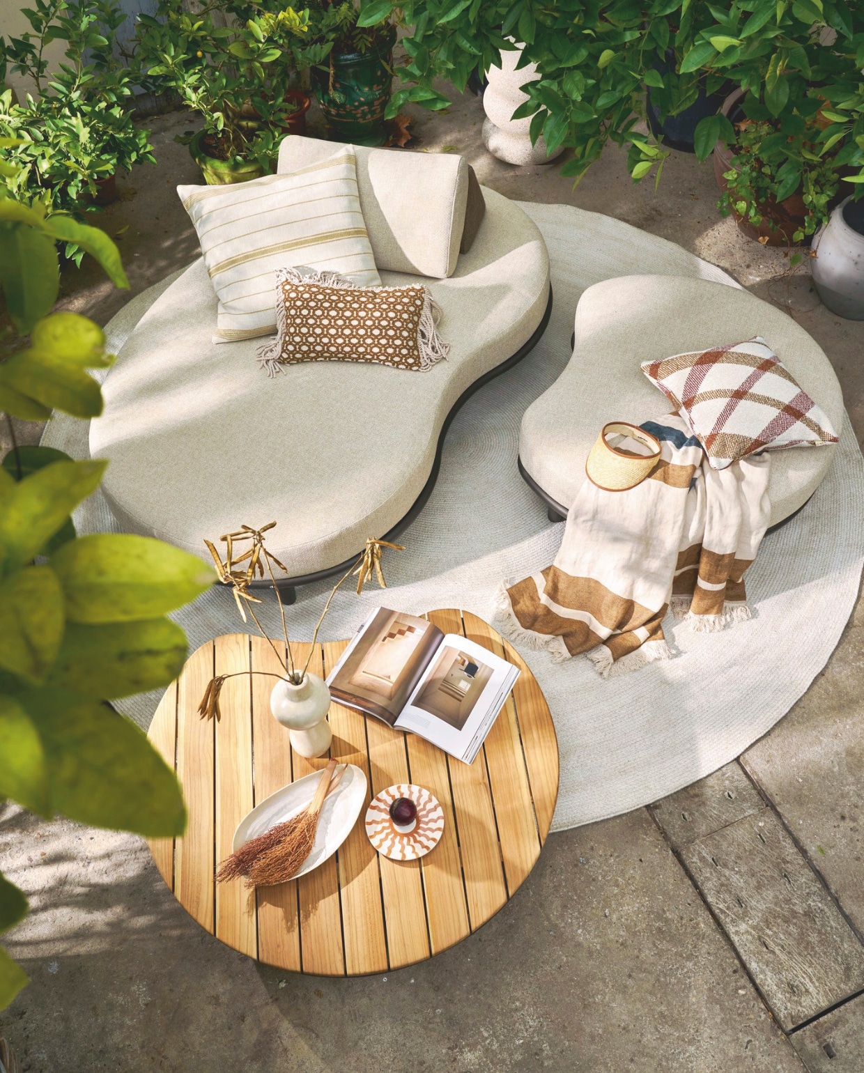 Apple Bee sofa Moon Island, olefin-stof en gepoedercoat aluminium frame, zandtint, 196x110x81 cm (lxbxh) € 1449,-,  poef Moon Island, 110x90x40 cm (lxbxh) € 669,-, salontafel Moon Island, gepoedercoat aluminium en teakhout, 110x97x24 cm (lxbxh) € 799,-, buitenkleed Swirl,  gerecycled pet, zand, 300 cm (Ø) € 759,- (applebee.nl). Omar buitenkussen Oxy, fijn gestreept, crème-bruin, inclusief vulling € 195,-, buitenkussen Oman, geruit, inclusief vulling € 165,-, kussen Odile met franjes, bruin-crème, fijne ruit, inclusief vulling € 165,- (omar-antwerp.be). Libeco deken Julian, linnen € 396,- (libecohomestores.eu). Household Hardware vaas Bubble, tadelakt € 115,-, bord Fez, keramiek € 15,-, Woood bijzettafel Laurel, magnesium, spikkels beige, 50x40x40 cm (lxbxh) € 99,95 (shop.vtwonen.nl). Overig privébezit. vtwonen 03-2026 | styling Cleo Scheulderman | fotografie Jeroen van der Spek