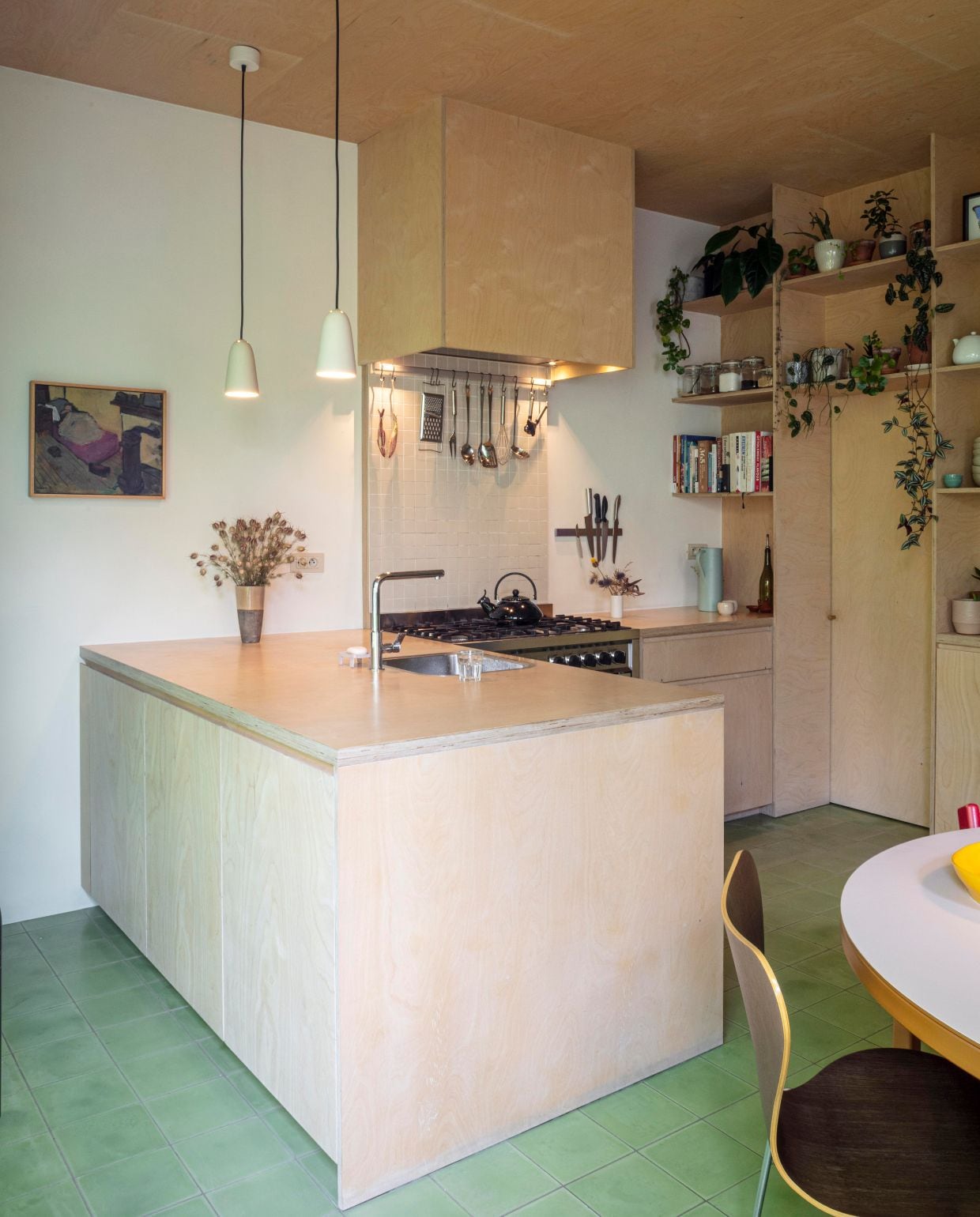 Groene cementtegels De Rocker Gent. Keuken en plafond zelfgemaakt van multiplex berk. Lampen Jos Devriendt. Keukenkraan Neptune van Franke. Tafel Atelier Janda Vanderghote. Vlinderstoel Fritz Hansen  Series 7 eikenfineer van Arne Jacobsen. Kunstwerk Laurens Janda. Theepot Le Creuset. Koffiekan Ikea. Zeepschaal Kleiduif Gent. Keramieken vissen uit Portugal. vtwonen 03-2026 | fotografie Tim van de Velde