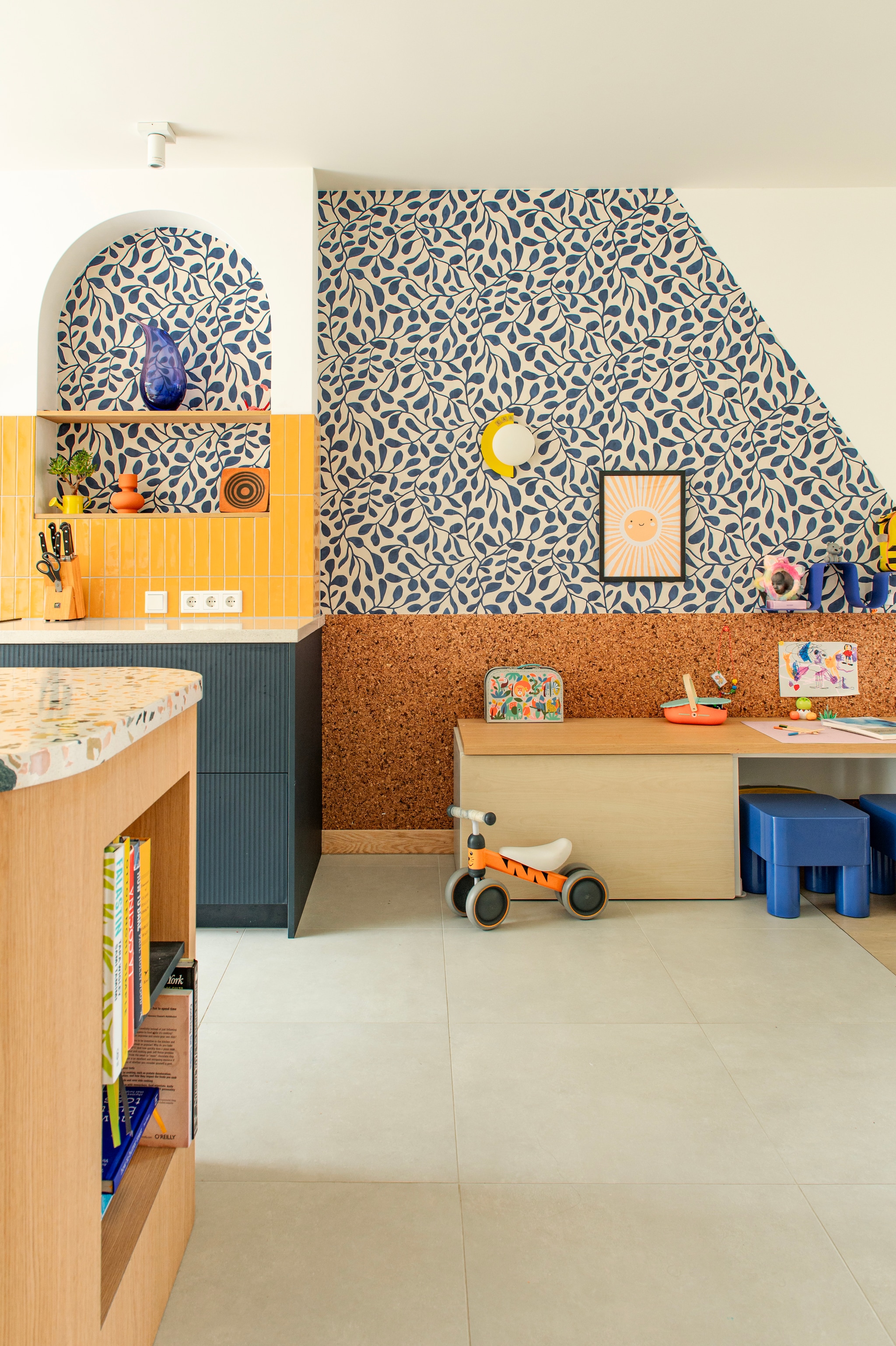 Behang Twist van Eijffinger. Kurkwand Kurk24. Speeltafel Ikea. Krukken Chubb en blauwe wandplank van Jotex. Poster Poster Store. Keuken Jorik Maakt. Tegels Luz Giallo van Marazzi. Muurkleur Wevet van Farrow & Ball. vtwonen 07-2026 | fotografie Caroline Coehorst