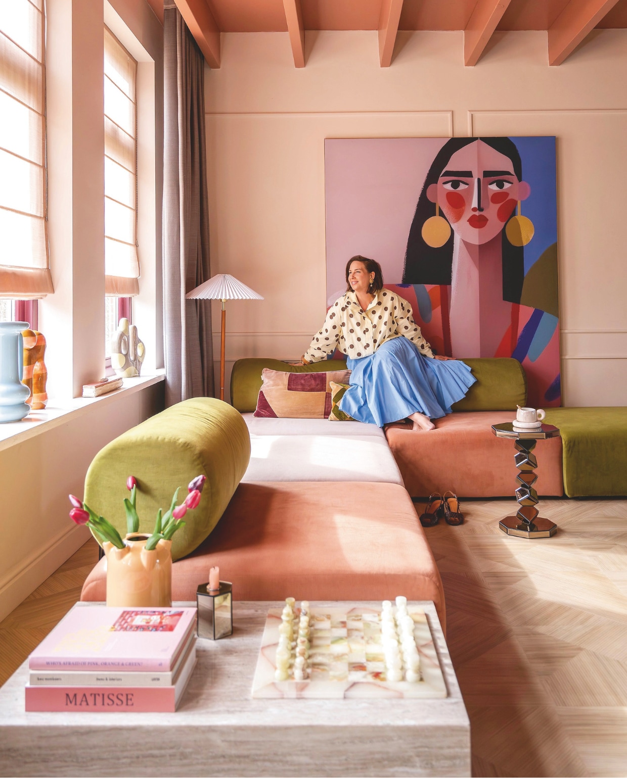 Bank Zitmaxx. Schilderij Carla Van Iersel via Werk aan de Muur. Staande lamp H&m Home. Blinds Kendix. Gordijnen De Ploeg. Vloer Moduleo. Hoektafels, blauwe vaas en spiegeltafel By-Boo. Schaakbord The Vintage Atelier. Kandelaars Kwantum. Kussens Sézane. Verfkleuren plafond Light Cherry Parade en wand Peach Pudding van Histor. vtwonen 07-2026 | fotografie Lotte van Uittert